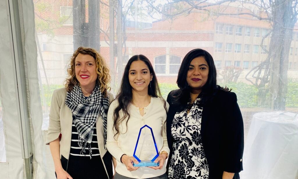 Heather Conner, Anam Khan, and Dr. Purna Gamage stand in front of a window while Anam holds her award