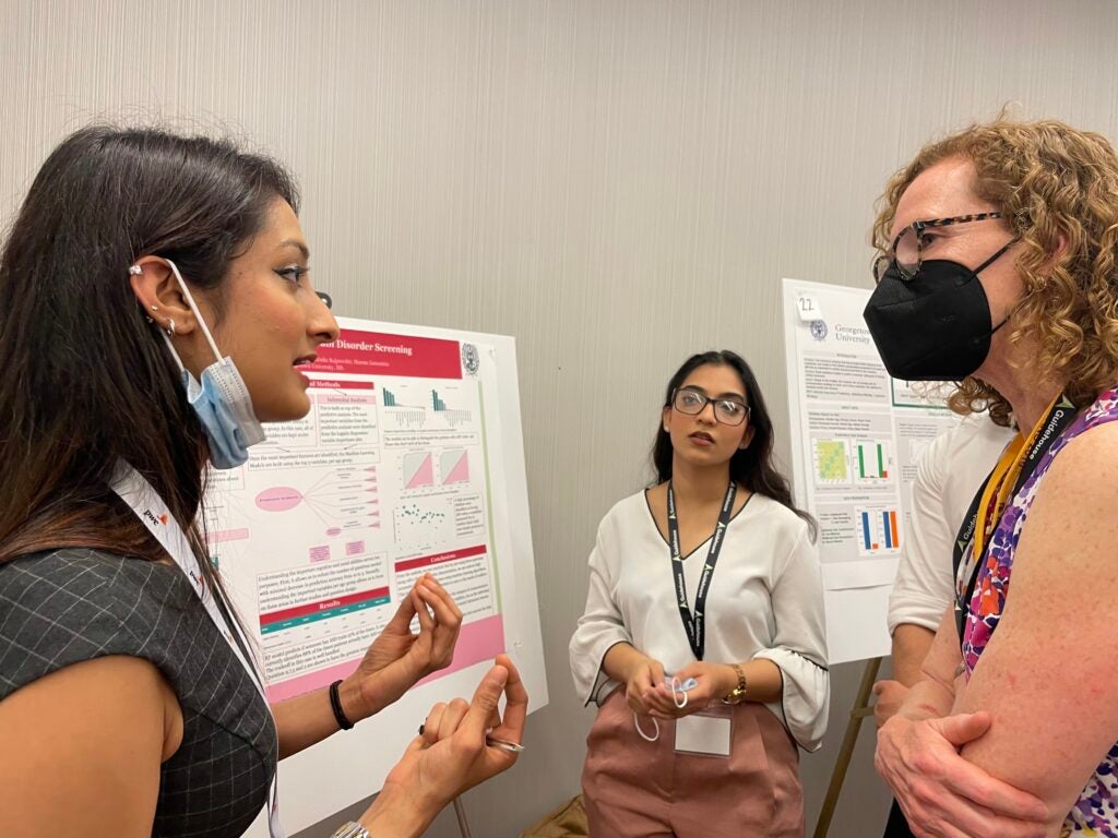 Our students explain their data visualization poster to an attendee.