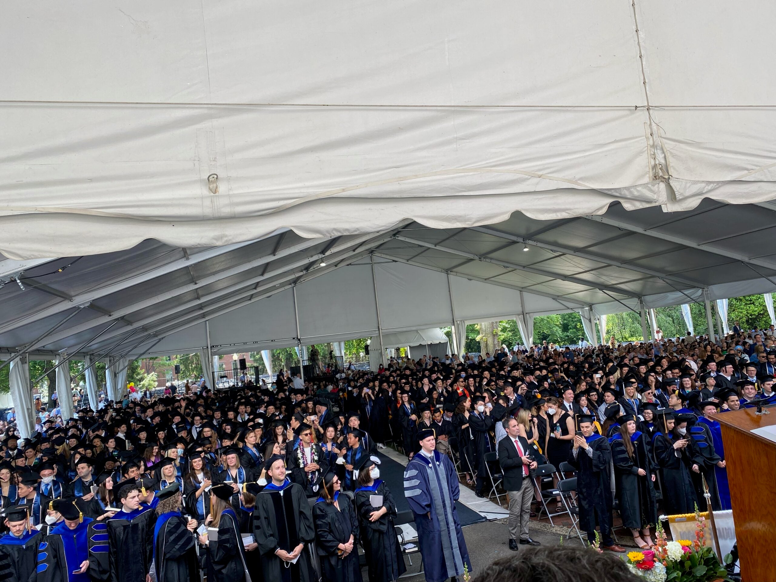 DSAN graduates seated in cap and gown gathered under white tent