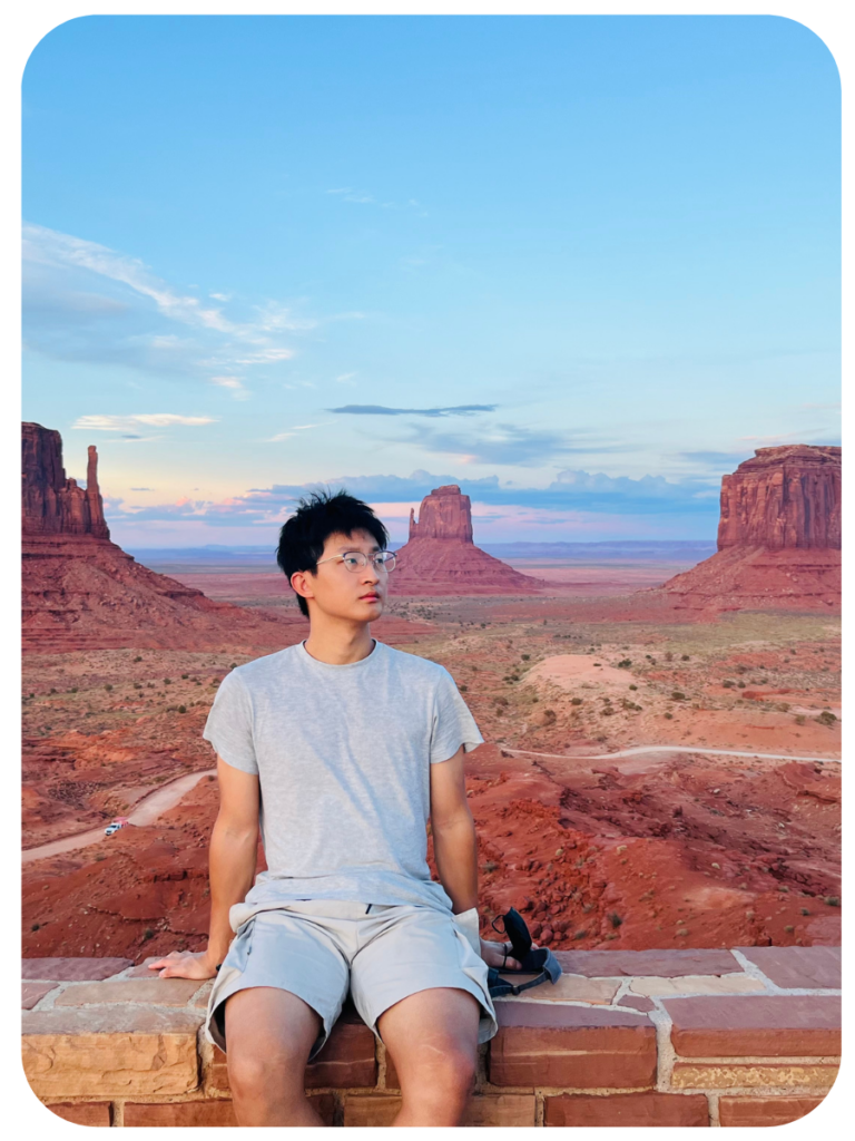 Chao Li sitting on a ledge in front of desert mountains.