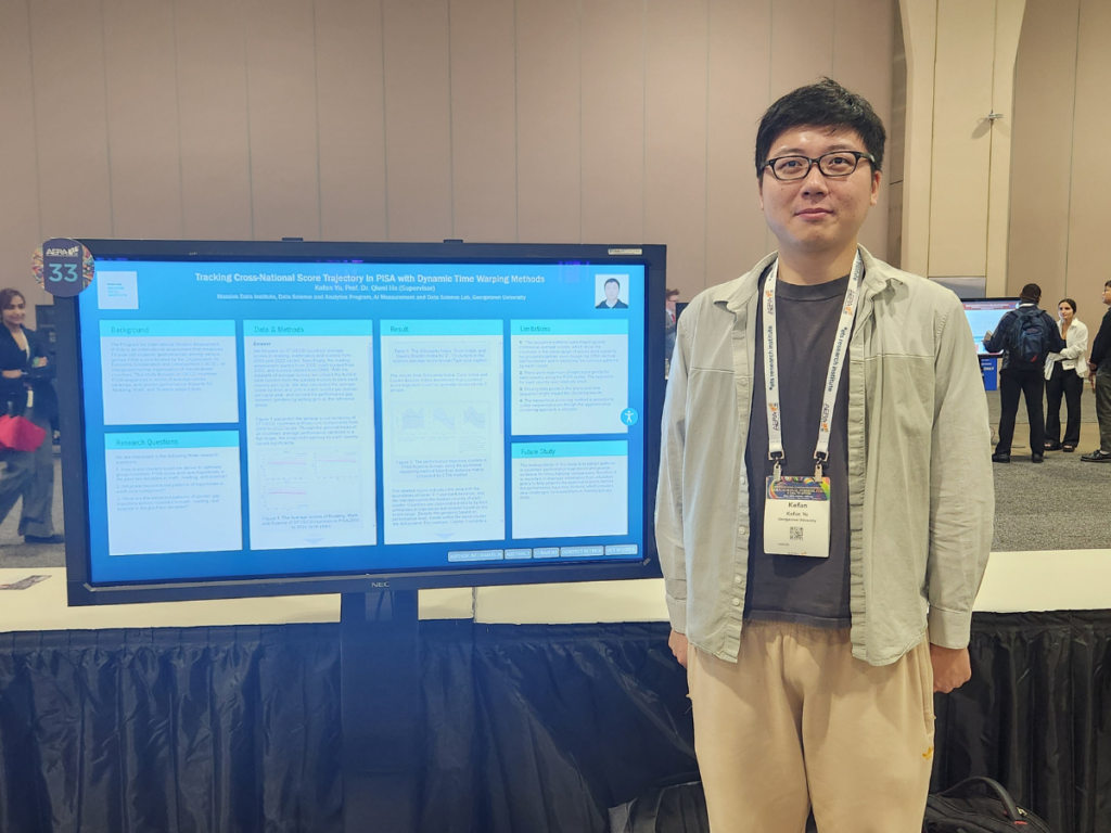 Kefan stands in a conference hall in from of a large digital monitor that is displaying his poster.