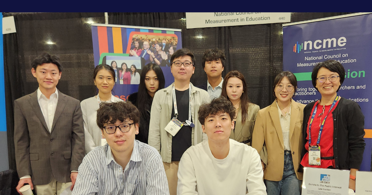 A group of students and Dr. Britt He stand behind a conference booth table facing the camera