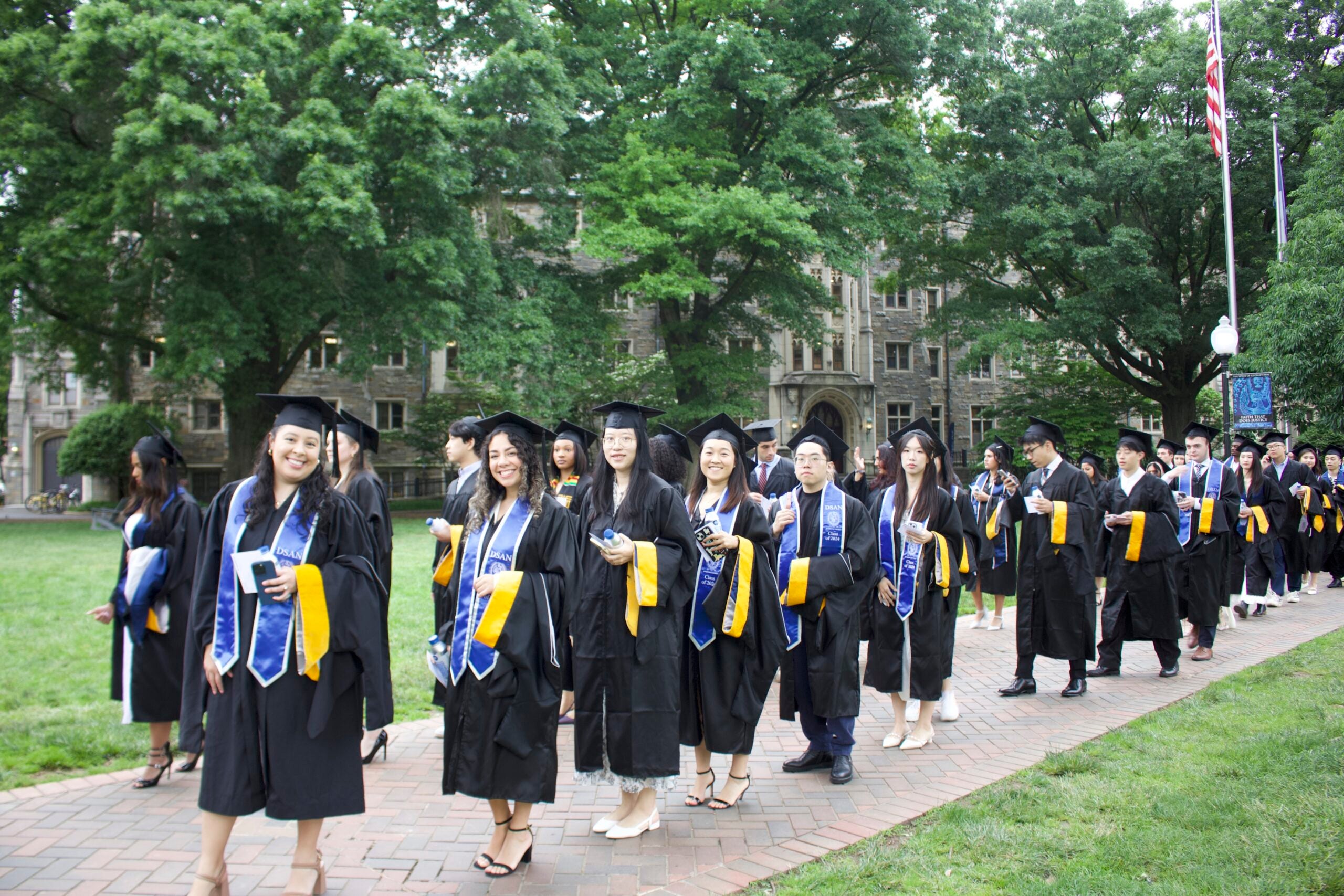 DSAN students walking through Healy Lawn in graduation regalia.