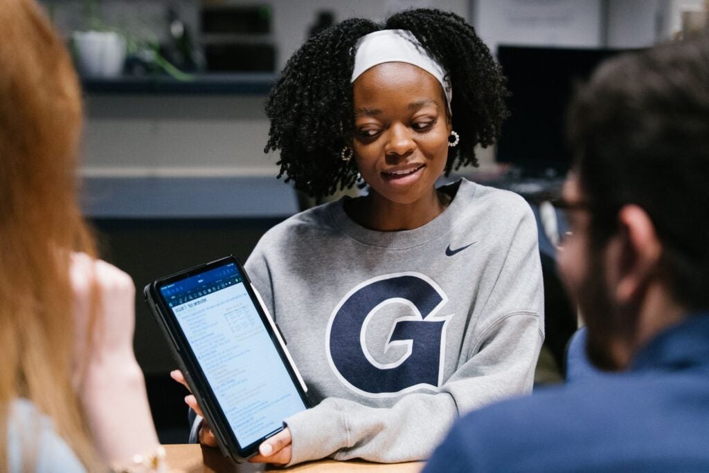 A student shows a tablet to two other students.
