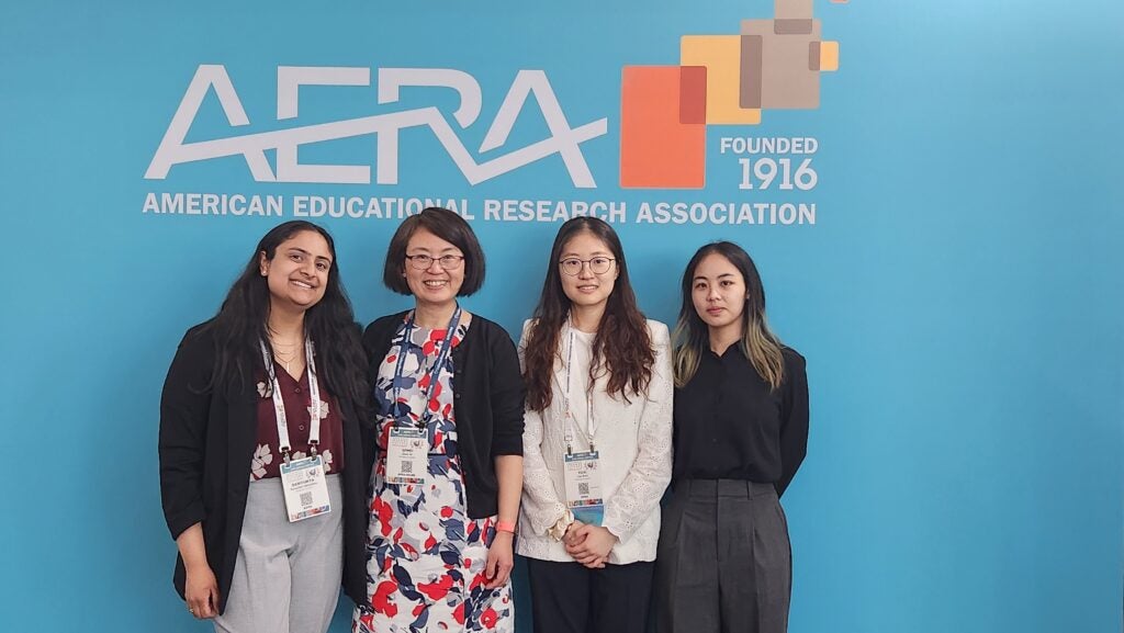 Dr. Britt He, Samyu, Yuxi, and Binhui pose in front of the AERA banner.
