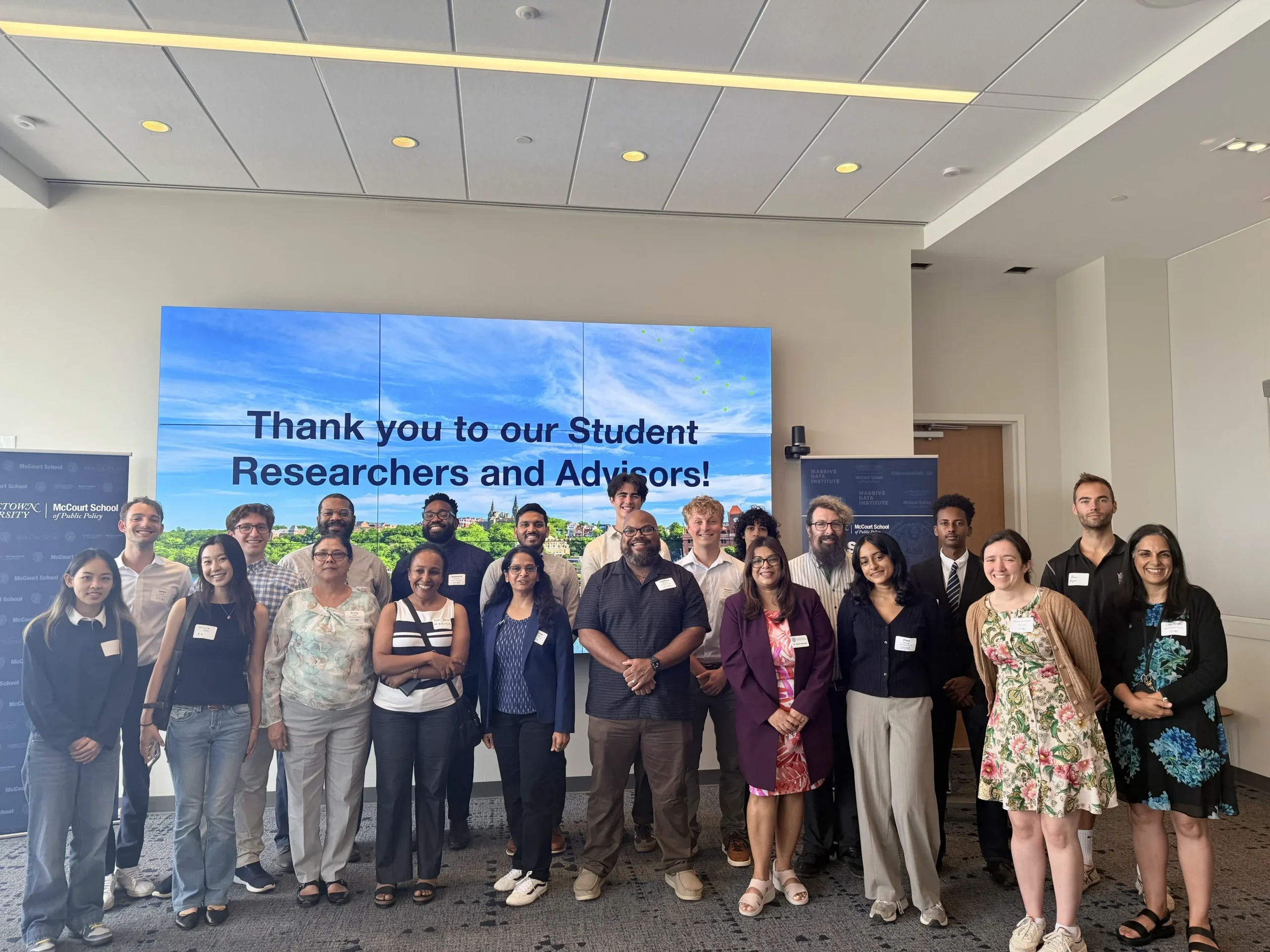 Student researchers and advisors pose in front of a screen thanking them for their work.